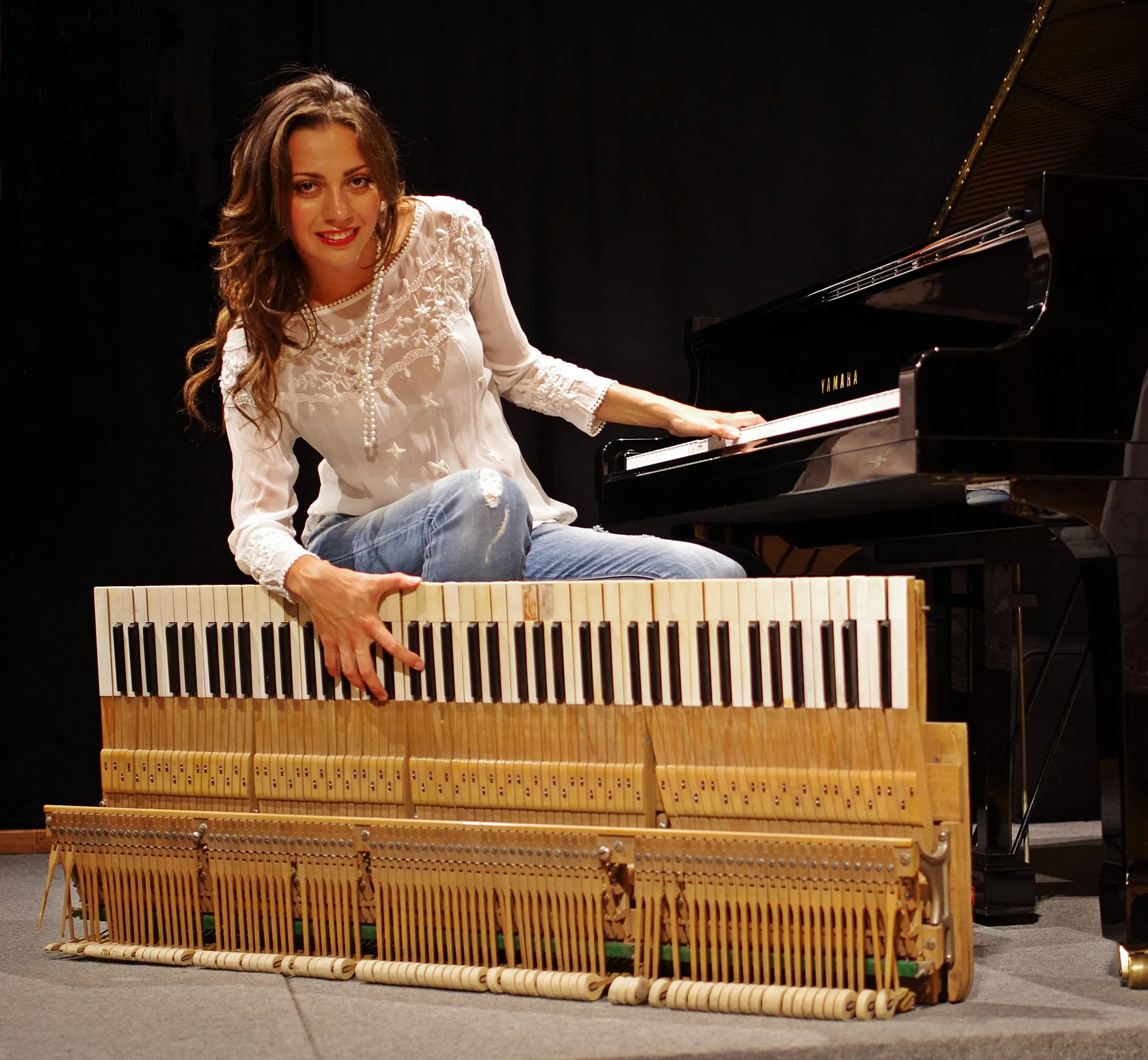 Valentina Dzhegnaradze sorride seduta accanto al suo pianoforte Yamaha, la mano sulla meccanica estratta: i tasti e i martelletti in fila